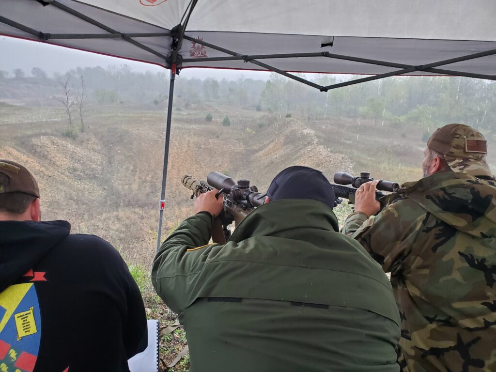 Participants using rifles beneath a canopy at an outdoor range